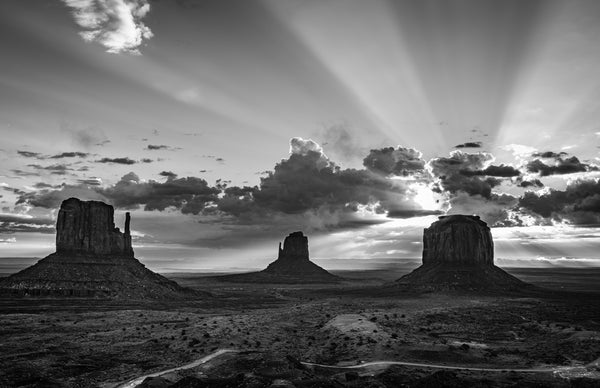 Black and white landscape of Monument Valley with sun rays through clouds
